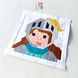 Könnte beinhalten: Ein quadratischer Stoff-Quiltblock mit einem verpixelten Charakterdesign eines Ritters, der einen grauen Helm mit gelbem Federbusch, braunes Haar und eine blaugrüne Tunika trägt. Das Design ist von einem weißen Rand umgeben und enthält den Text.