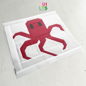 May include: A white fabric panel with a red octopus applique. The octopus is made of fabric squares and has a simple, geometric design.
