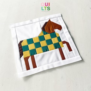 Pode incluir: Um bloco de colcha quadrado com um design de cavalo feito de peças em castanho, amarelo e azul-petróleo, sobre um fundo branco. O cavalo tem cabeça e pernas castanhas, com um corpo axadrezado amarelo e azul-petróleo. O texto QUILTS AND NICE STUFF é visível.
