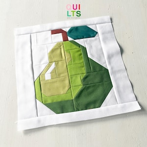 Könnte beinhalten: Ein quadratischer Quiltstoff mit einem geometrischen Birnenmuster in Grüntönen, mit einem braunen Stiel und einem türkisfarbenen Blatt. Die Birne ist vor einem weißen Hintergrund platziert, mit dem Text "QUILTS AND NICE STUFF" in der oberen rechten Ecke.