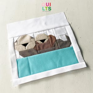 May include: A white fabric square with a blue fabric rectangle sewn on the bottom. The top of the square has a brown and white fabric design of two sea otters.