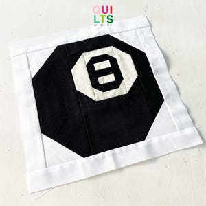 May include: Black and white quilt block with a white number eight in the center. The block is surrounded by a white border.