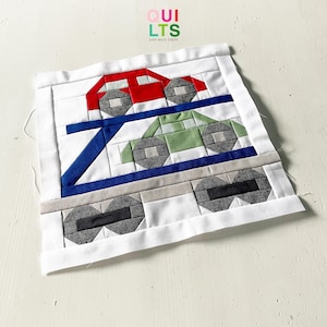 Könnte beinhalten: Handgefertigtes Quiltquadrat mit einem Design von roten und grünen Autos. Die Autos sind auf einem weißen Hintergrund mit blauen und grauen Akzenten platziert. Der Text "QUILTS AND NICE STUFF" befindet sich in der oberen rechten Ecke.