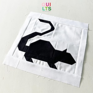 Könnte beinhalten: Ein handgefertigter Quiltblock mit einem schwarzen geometrischen Rattenmuster auf weißem Hintergrund. Die Ratte besteht aus eckigen Formen mit einem langen Schwanz. Der Block hat einen weißen Rand. Der Text "QUILTS AND NICE STUFF" befindet sich oben rechts.