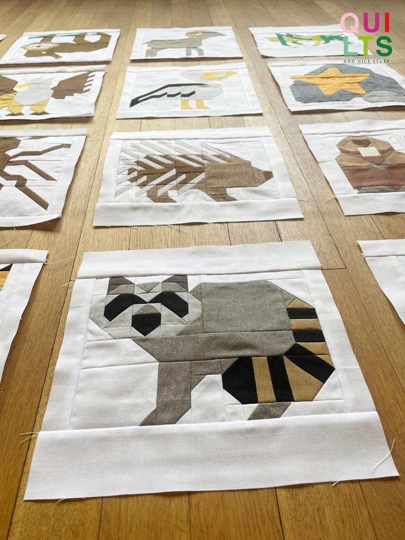 May include: A collection of 10 fabric squares featuring different animal designs. Each square is made of white fabric with a colourful animal design in the centre. The animals include a monkey, a deer, a bird, a star, a porcupine, a bear, a raccoon, a fox, a cat, and a dog.