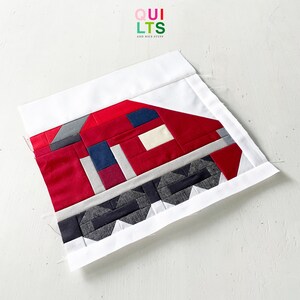 May include: A handmade quilt block featuring a geometric design in red, gray, navy, and white fabrics. The block has a rectangular shape with a white border and the text "QUILTS AND NICE STUFF" in the upper right corner.