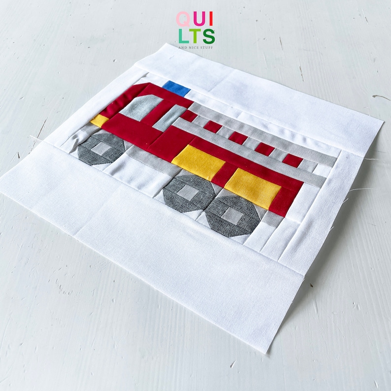 K&ouml;nnte beinhalten: Ein handgefertigter Quiltblock mit einem Feuerwehrwagen-Design. Der Feuerwehrwagen ist haupts&auml;chlich rot, mit gelben, grauen und silbernen Akzenten. Der Block ist von einem wei&szlig;en Rand umgeben. Der Text "QUILTS AND NICE STUFF" ist sichtbar.