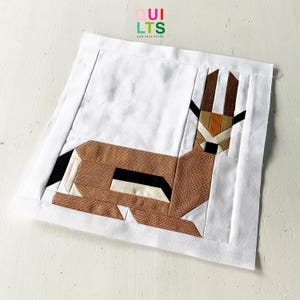 Könnte beinhalten: Ein brauner und weißer geometrischer Patchwork-Quiltblock mit einem stilisierten Tierdesign. Der Block besteht aus verschiedenen Brauntönen, Weiß und Schwarz.