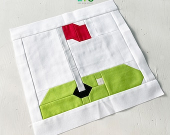 Peut inclure: Un carré de tissu blanc avec une applique verte et rouge représentant un drapeau de golf. Le carré de tissu a une bordure blanche et le texte "QUI LTS AND NICE STUFF" est imprimé en haut au centre.