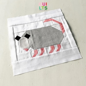 Könnte beinhalten: Ein weißer Stoffquadrat mit einem rosafarbenen und grauen Patchwork-Design eines Opossums. Der Stoffquadrat hat einen weißen Rand und der Text "QUI LTS AND NICE STUFF" ist in der oberen linken Ecke gedruckt.