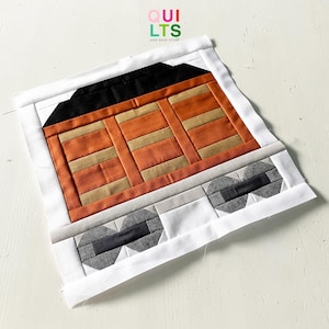 Könnte beinhalten: Ein handgefertigter Quiltblock mit einem Eisenbahnwaggon-Design. Der Block verwendet orangefarbenen, beigen, schwarzen, grauen und weißen Stoff. Auf der Oberseite des Blocks steht der Text "QUILTS AND NICE STUFF" in Grün, Rot und Weiß.