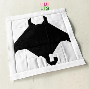 Könnte beinhalten: Ein schwarzer und weißer Quiltblock mit einem geometrischen Design einer Mantarochen. Der Block besteht aus Stoffquadraten, die zusammengenäht werden, um die Form des Rochens zu bilden.