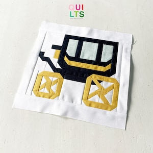 Può includere: Un blocco di tessuto per trapunte quadrato con un design a pezzi raffigurante una carrozza in nero, giallo senape e verde pallido su sfondo bianco. Il testo QUILTS AND NICE STUFF è stampato in piccole lettere al centro del bordo in tessuto bianco.