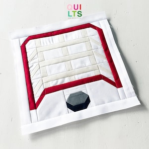 May include: A geometric quilt block featuring a white background with red and beige accents. The design includes a red border, a gray geometric shape, and the text "QUILTS AND NICE STUFF" in the upper right corner.