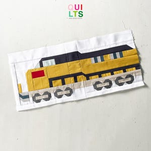 Könnte beinhalten: Ein handgefertigter Quiltblock mit einem gelben, schwarzen und roten Zugdesign. Der Zug hat graue Räder und ist vor einem weißen Hintergrund platziert. Der Text "QUILTS AND NICE STUFF" befindet sich in der oberen rechten Ecke.