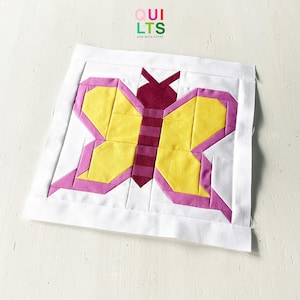 May include: A patchwork quilt block with a butterfly design. The butterfly has yellow wings with pink borders, a pink and burgundy body, and burgundy antennae. The block is set against a white background. The text "QUILTS AND NICE STUFF" is in the upper right corner.
