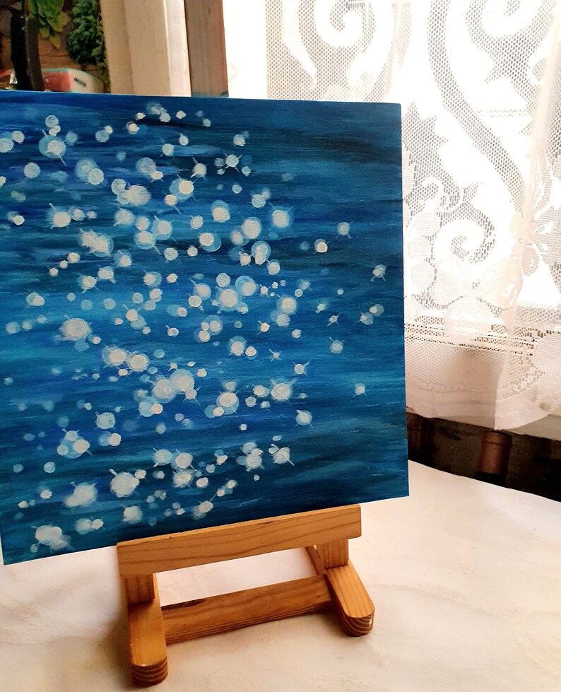 May include: An abstract painting on canvas, featuring a deep blue background with white, circular brushstrokes. The artwork is displayed on a small wooden easel, creating a gallery-like presentation. The painting evokes a sense of depth and movement.
