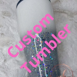 May include: A white and silver glitter tumbler with the words "Custom Tumbler" in pink lettering.
