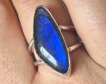 Peut inclure: Une bague en argent avec une grande pierre précieuse bleue irisée sertie dans une forme ovale pointue.