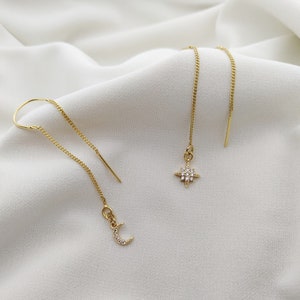 May include: A pair of gold dangle earrings with a crescent moon and a star charm. Both charms are adorned with small, clear crystals.