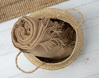 May include: A brown woven basket with a brown blanket or throw inside. The basket has two handles.