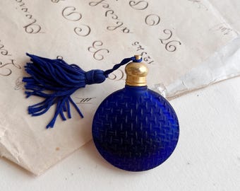 Klein rond parfumflesje van ondoorzichtig blauw matglas en messing dop met blauw kwastje. Verzamelobject parfumflesje.