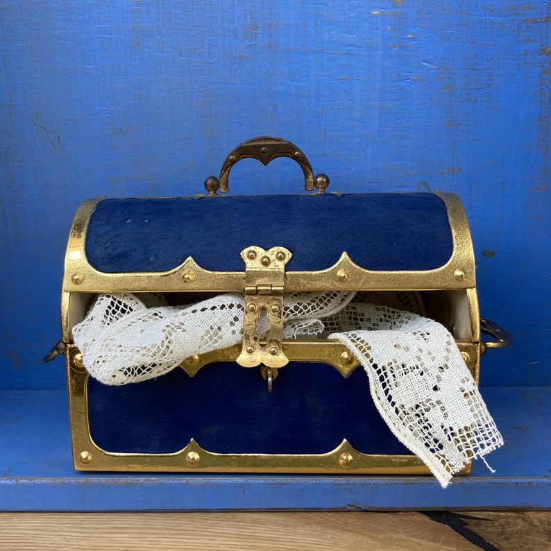 May include: A blue velvet treasure chest with gold accents and a delicate lace doily inside. The chest has a hinged lid and a decorative lock.