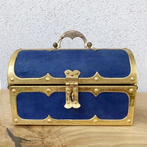 May include: A small, blue velvet treasure chest with gold accents and a hinged lid. The chest has a decorative lock and a metal handle.