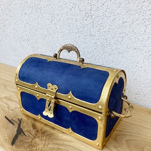 May include: A blue velvet treasure chest with gold accents and a hinged lid. The chest has a decorative brass handle and a lock.