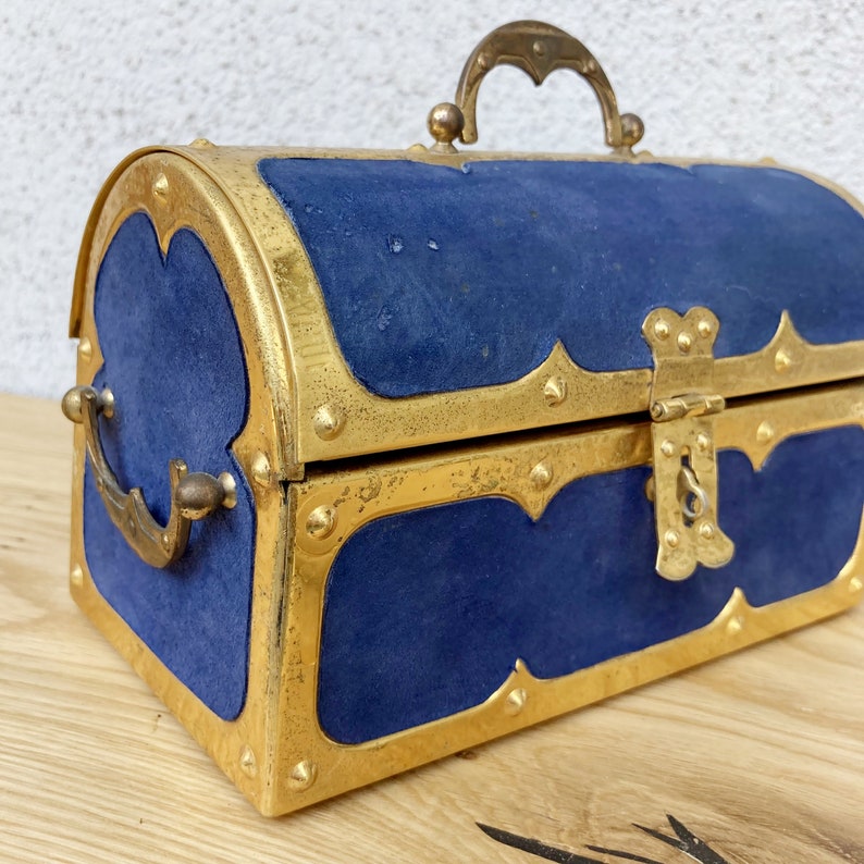 May include: A blue velvet treasure chest with gold accents and a brass lock. The chest has a hinged lid and a carrying handle.