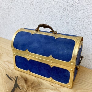 May include: A blue velvet treasure chest with gold accents and a brass handle. The chest has a hinged lid and a decorative design.