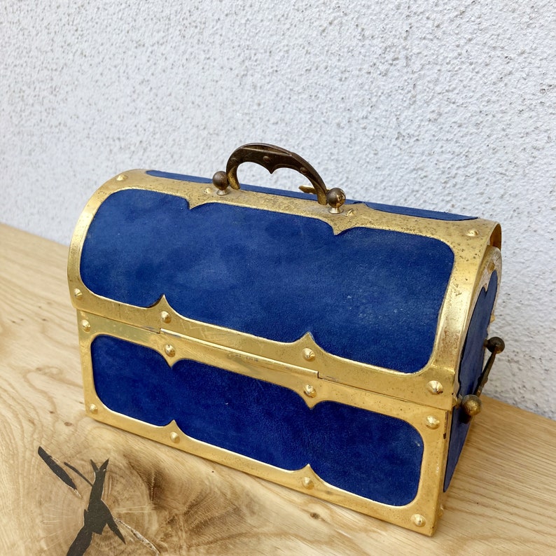 May include: A blue velvet treasure chest with gold accents and a brass handle. The chest has a hinged lid and a decorative design.