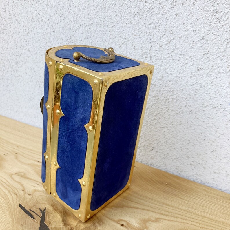 May include: A blue velvet jewelry box with gold trim and a decorative metal handle.