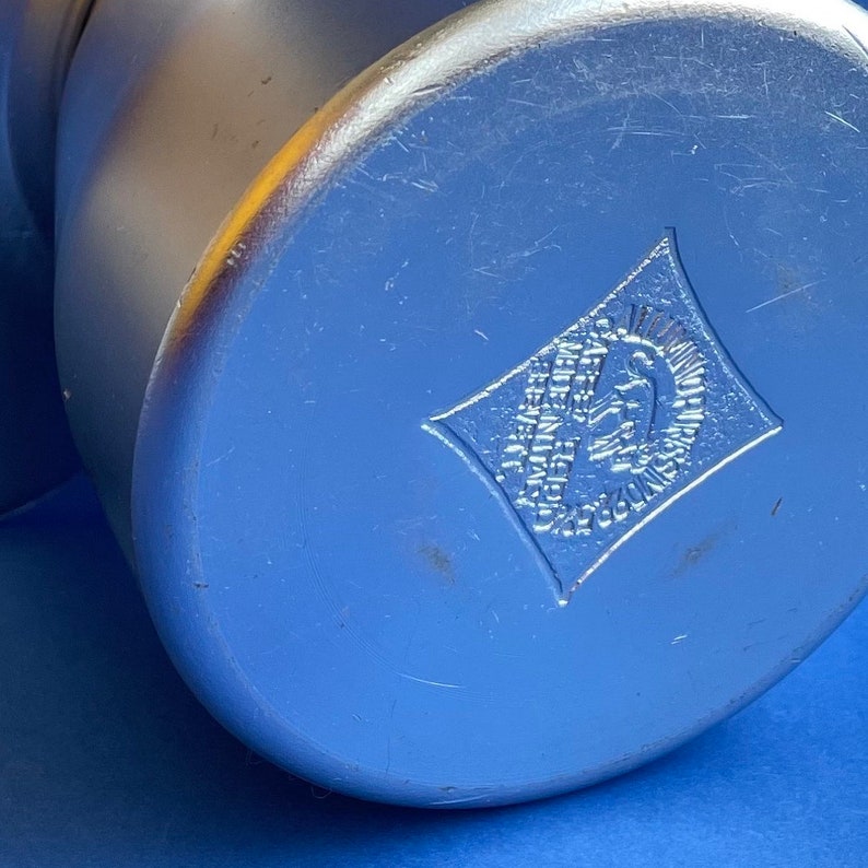 Op de afbeelding: Een zilveren metalen container met een ruitvormig logo met de tekst "E.G.M.M.  MADE IN GERMANY  REG. U.S. PAT. OFF."