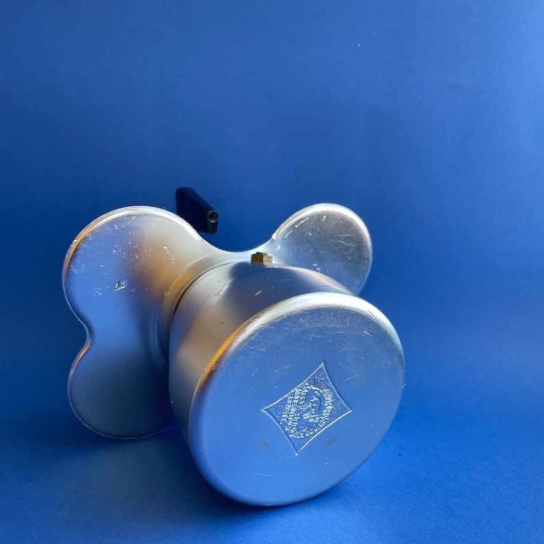 Op de afbeelding: Zilveren aluminium koffiezetapparaat met een zwart handvat en een ruitvormig logo met de tekst "Bialetti".