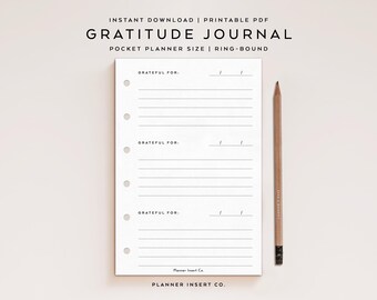 May include: A white ring-bound gratitude journal with lined pages and the text "GRATITUDE JOURNAL". A wooden pencil rests beside the journal. The journal includes the text "GRATEFUL FOR:" and is labeled "POCKET PLANNER SIZE | RING-BOUND".