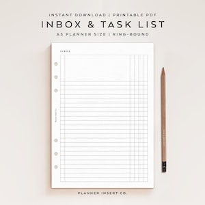 May include: A white A5 planner insert with the text "INBOX & TASK LIST" and "INBOX" printed on it. The insert has a grid layout with horizontal and vertical lines. A wooden pencil rests on the right side of the insert.
