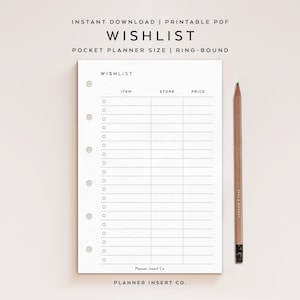 May include: A white wishlist planner insert with a grid for items, stores, and prices. The text "WISHLIST" is at the top. A wooden pencil rests on the right. The planner is ring-bound and pocket-sized.