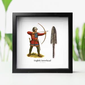 May include: Framed print featuring an illustration of an English archer with a bow and arrow, alongside a detailed image of an arrowhead. The archer is dressed in red and blue attire. The text "English Arrowhead" is displayed below the images.