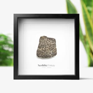 May include: A framed piece of Neolithic pottery, a dark gray shard with a rough texture, displayed on a white background. The text "Neolithic Pottery 7500BC - 5000BC" is printed below the shard.