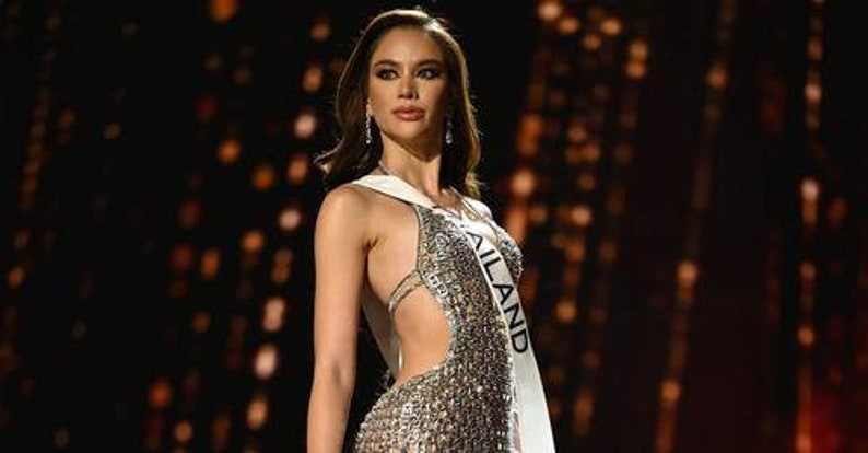 May include: A woman wearing a silver sequined gown with a sash that reads "THAILAND".