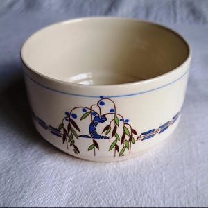 Puede incluir: Cuenco de cerámica color crema con un diseño floral azul y verde. El cuenco tiene una banda azul alrededor del borde y un patrón decorativo de hojas y bayas estilizadas. Un artículo de cocina vintage.