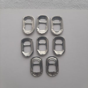 May include: Eight silver pull tabs from aluminum beverage cans. The tabs are arranged in three rows, with three tabs in the top row, three tabs in the middle row, and two tabs in the bottom row.