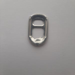 May include: A silver pull tab from a can, isolated on a white background.