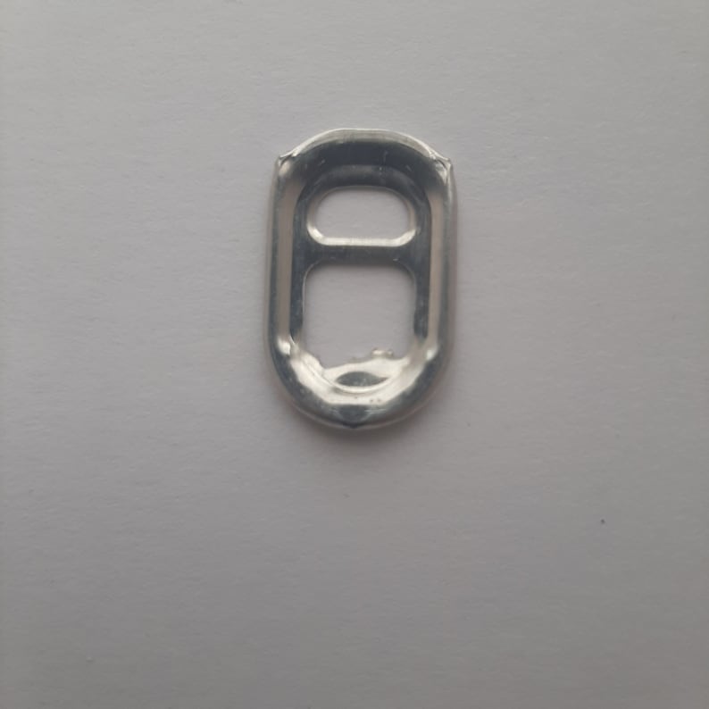 May include: A silver pull tab from a can, isolated on a white background.