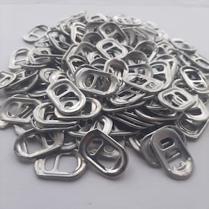 May include: A large pile of silver pull tabs from aluminum beverage cans. The tabs are all in various positions, some are stacked on top of each other, and some are spread out.