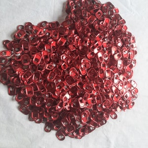 May include: A large pile of red metal pull tabs. The tabs are all the same size and shape, and they are arranged in a random pattern.