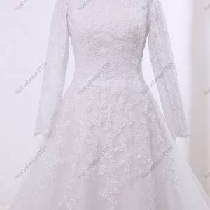 May include: A white wedding dress with long sleeves and a lace bodice. The skirt is made of tulle and has a flowing silhouette.