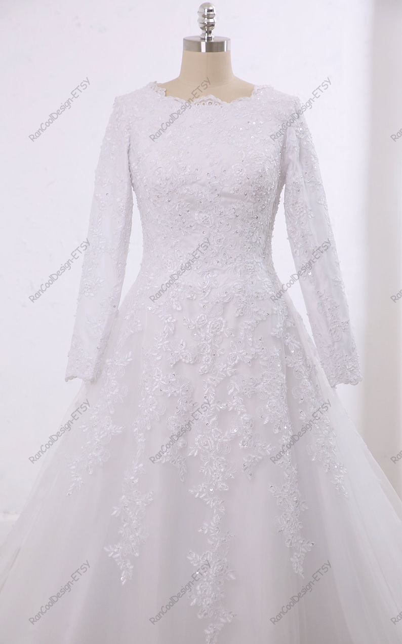 May include: A white wedding dress with long sleeves and a lace bodice. The skirt is made of tulle and has a flowing silhouette.