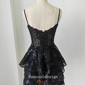 May include: Black short dress with a layered skirt and lace detailing. The dress has a fitted bodice and spaghetti straps. The dress is made of a sheer fabric with sequins throughout. The dress is shown on a mannequin. The text "Rancooldesign Etsy" is visible on the dress.